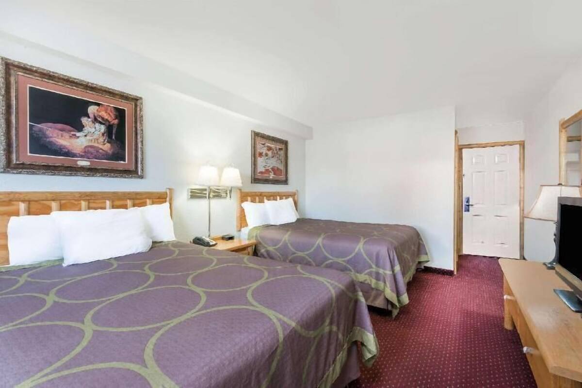 A hotel room with two beds, a desk, a television, and two framed pictures on the wall.