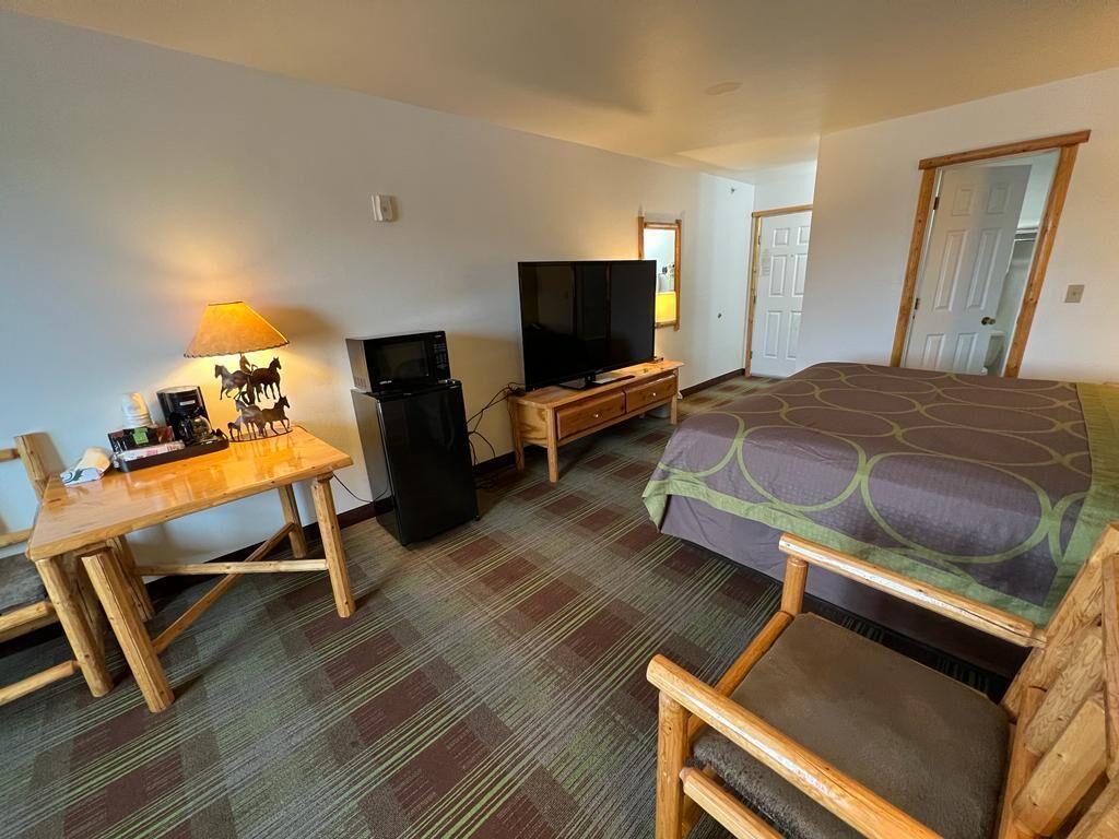 A hotel room with a bed, a TV, a desk with a lamp, and a chair.