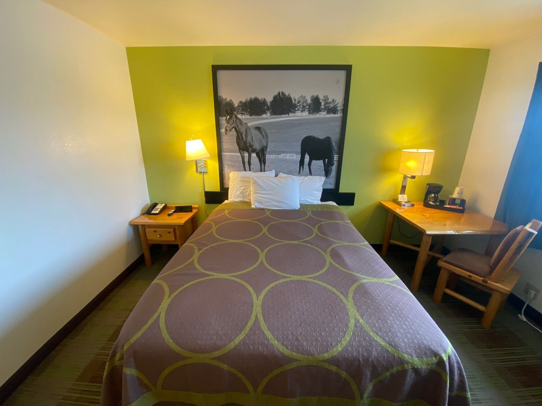Habitación de hotel con cama, dos mesitas de noche, escritorio, silla y lámpara de pared.