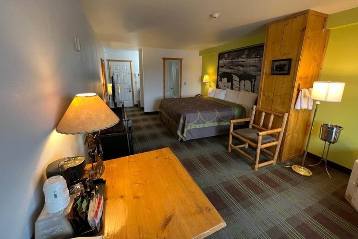 A hotel room with a bed, a wooden chair, a table, and a lamp.