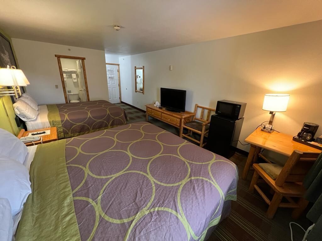 Habitación de hotel con dos camas, un televisor, un escritorio con lámpara y un microondas.