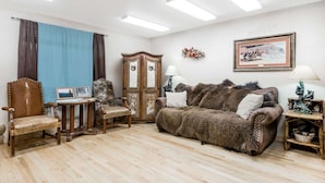 A living room with a wooden floor, a brown leather sofa, a wooden chair, a small table with a picture frame, a wooden cabinet, and a lamp.