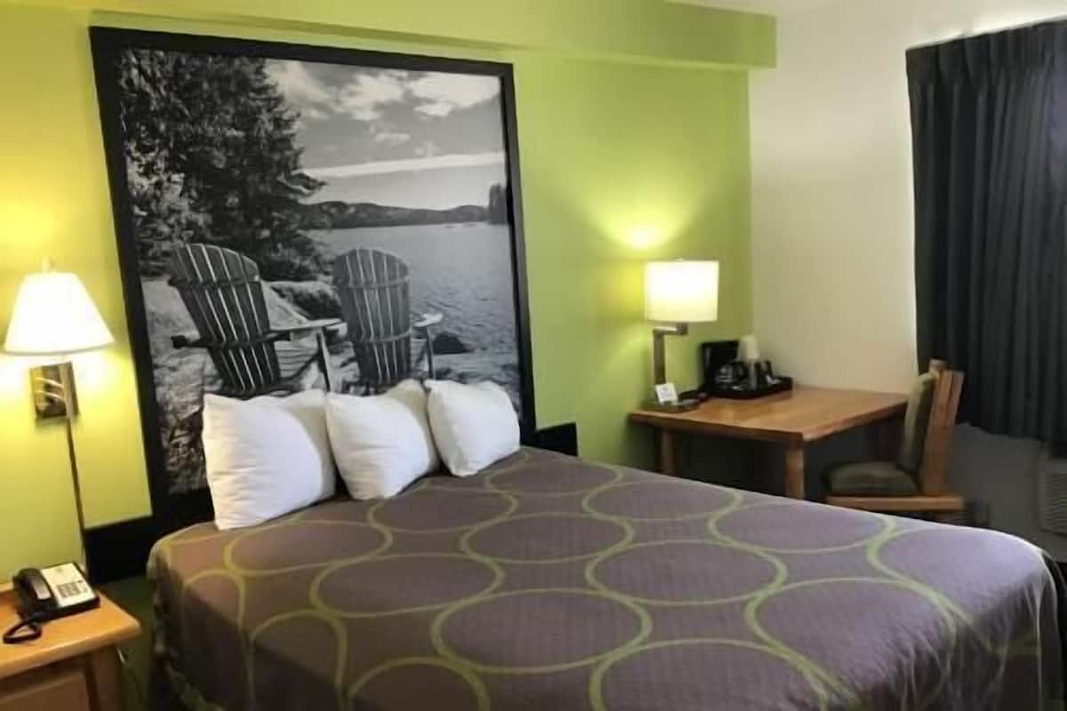 A hotel room with a bed, two bedside lamps, a desk with a chair, a telephone, and a large wall poster.