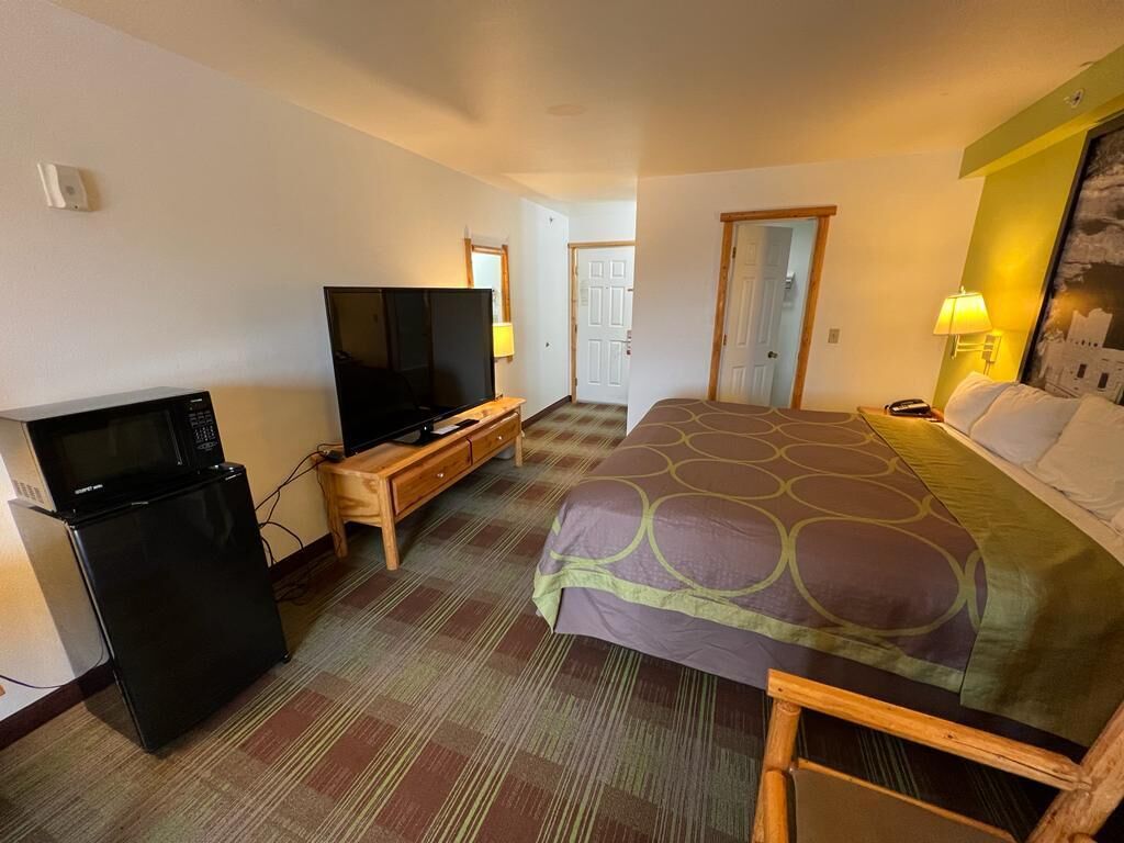 Habitación de hotel con cama, televisor, refrigerador y escritorio.