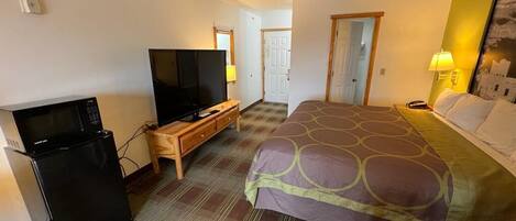A hotel room with a bed, a television, a refrigerator, and a desk.