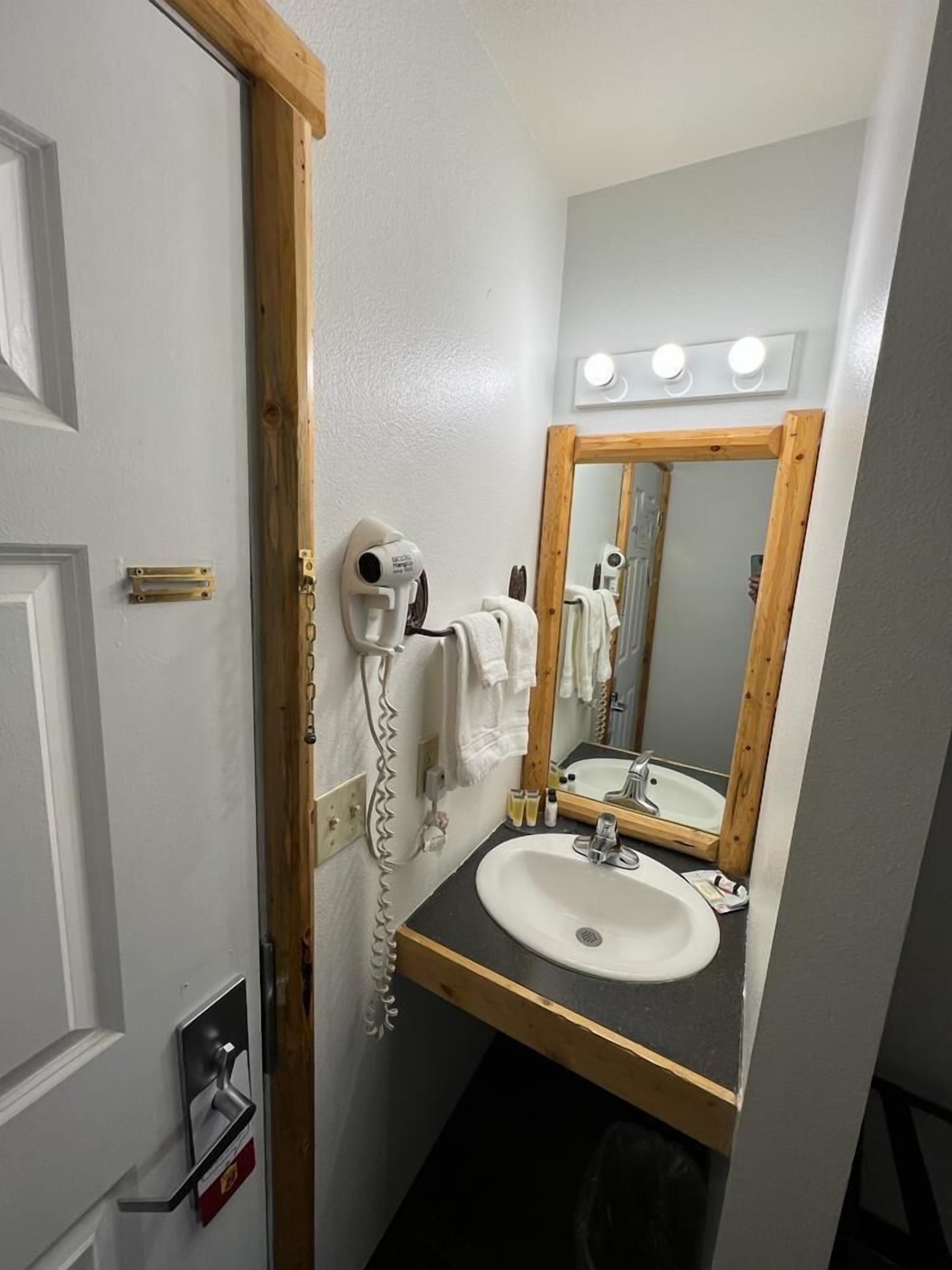 A bathroom with a white sink, a mirror with a wooden frame, a hairdryer, and a towel rack.