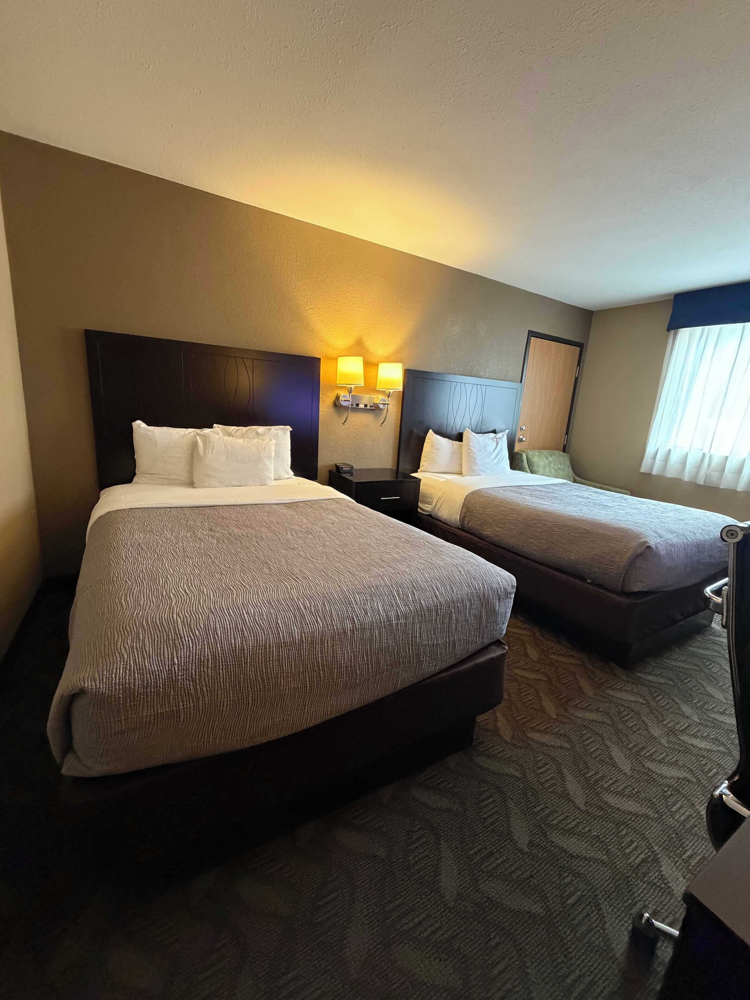 A hotel room with two beds, a nightstand, and a seating area.