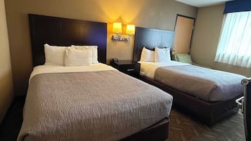 A hotel room with two beds, a nightstand, and a seating area.
