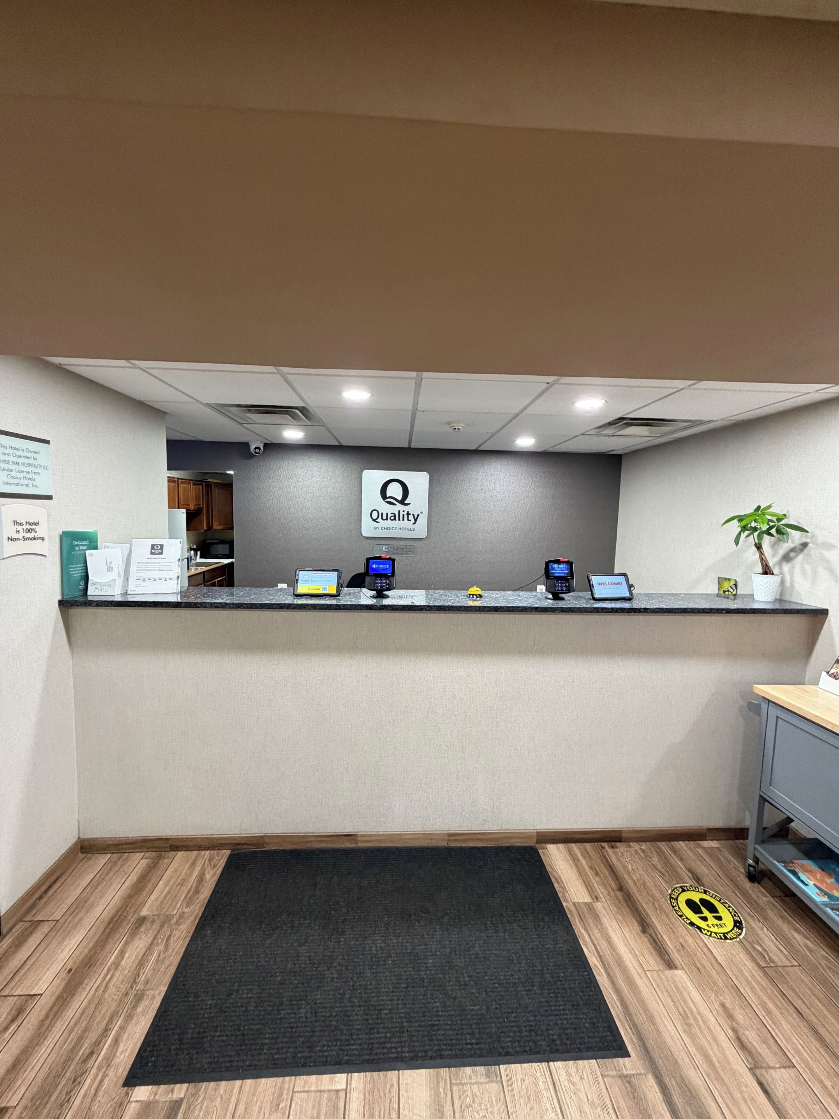 A hotel reception desk with a 'Quality by Choice Hotels' sign, a computer, a phone, and a small plant.