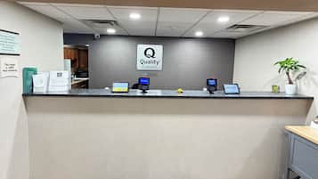 Een hotel receptiebalie met een 'Quality by Choice Hotels' bord, een computer, een telefoon en een kleine plant.