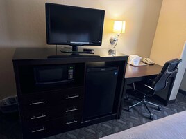 Habitación de hotel con televisión de pantalla plana, minibar, microondas, escritorio con lámpara y una silla.