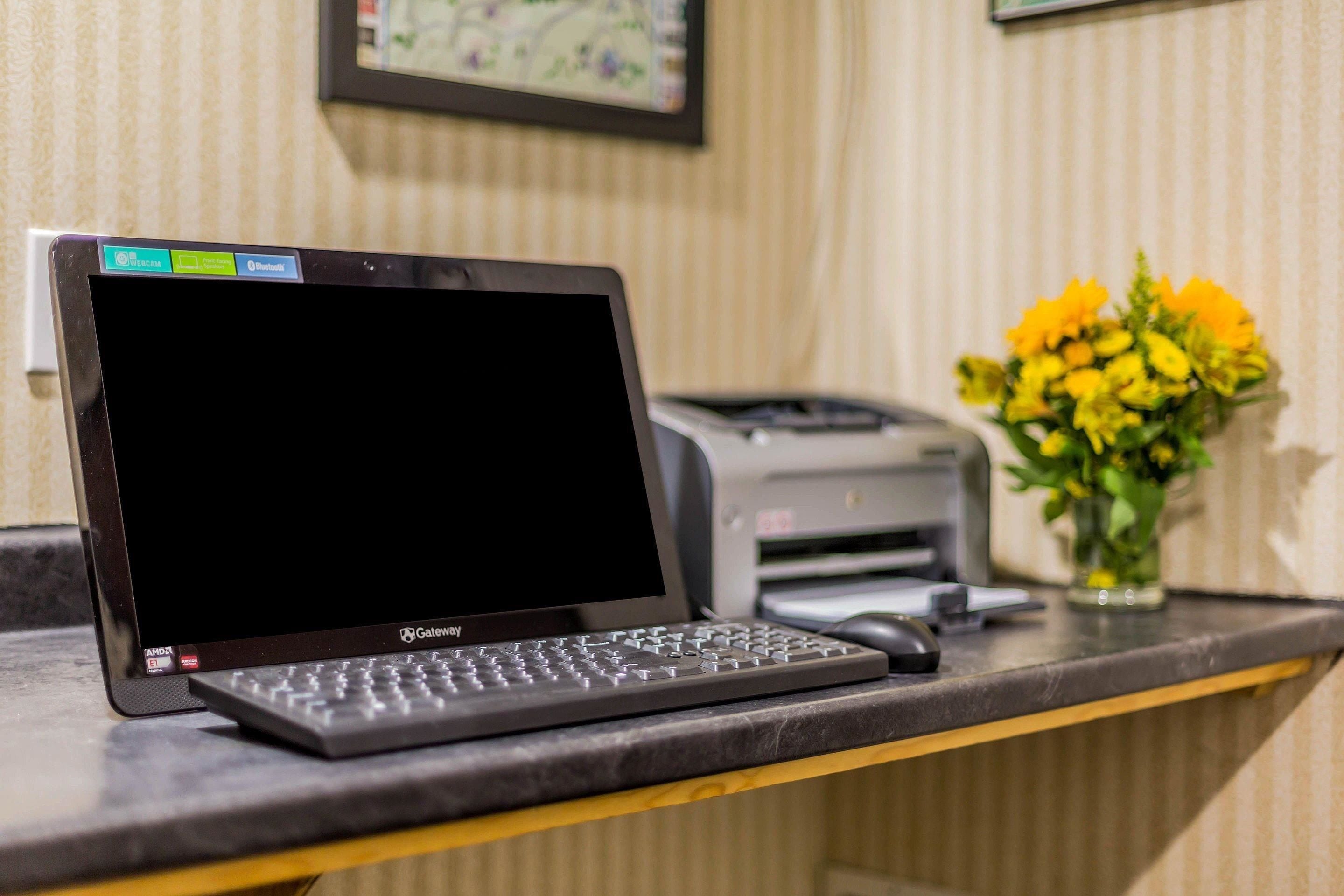 A laptop on a desk with a printer and a vase of flowers in the background.