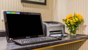 Un ordinateur portable sur un bureau, avec une imprimante et un vase de fleurs en arrière-plan.