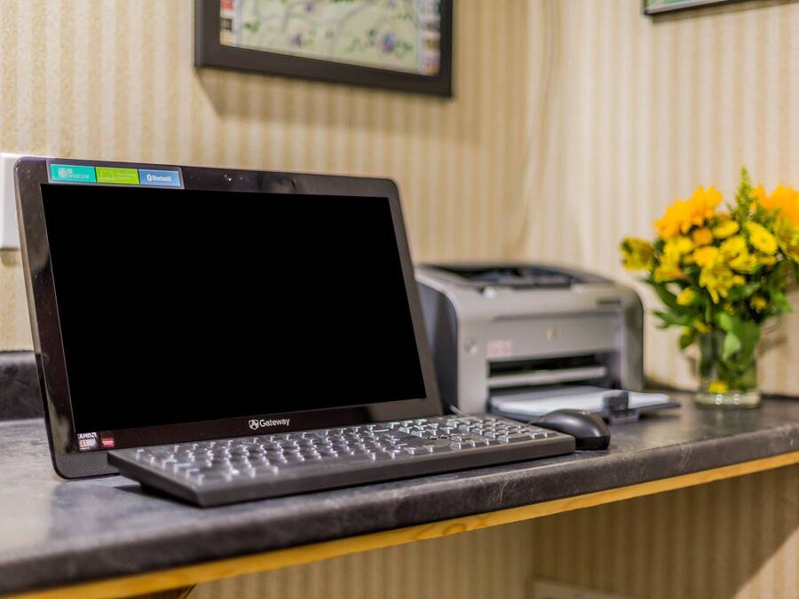 Een laptop op een bureau, met een printer en een vaas bloemen op de achtergrond.