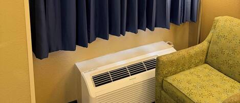 A room with a large window covered by dark blue curtains, a standing heater, and a green armchair.