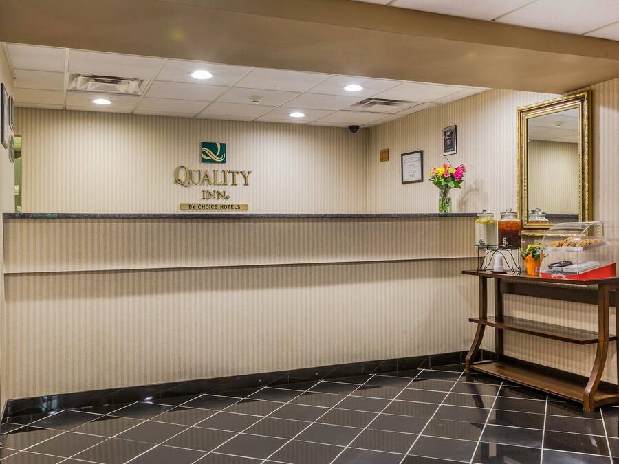 Aula, jossa on kyltti, jossa lukee «Quality Inn by Choice Hotels», vastaanottotiski, peili ja pieni pöytä, jonka päällä on joitain esineitä.