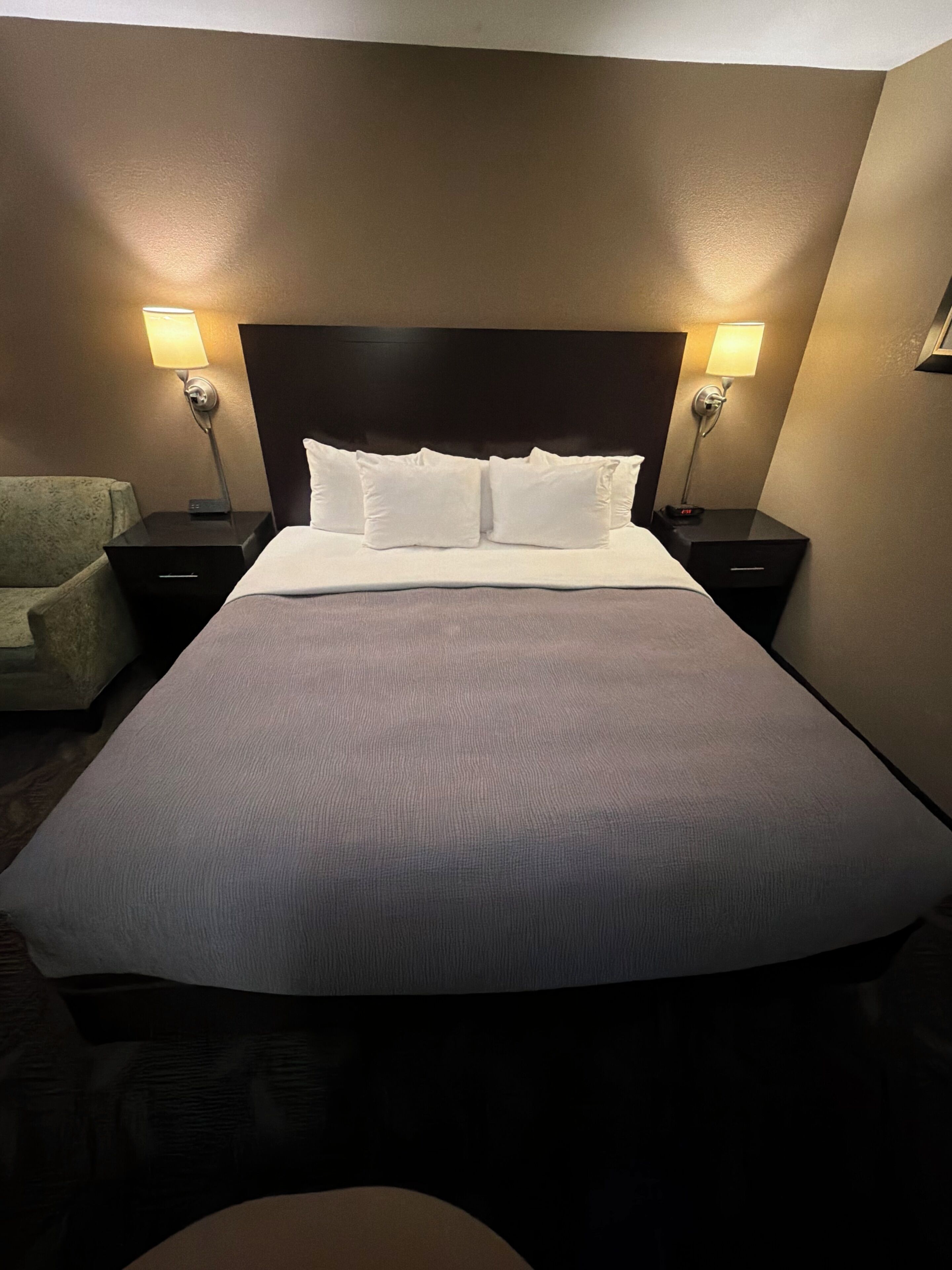A hotel room with a large bed, two bedside tables, a nightstand, and a chair.