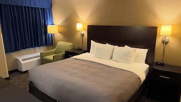A hotel room with a large bed, two bedside lamps, a chair, a heater, and a window with curtains.