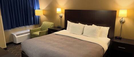 A hotel room with a large bed, two bedside lamps, a chair, a heater, and a window with curtains.