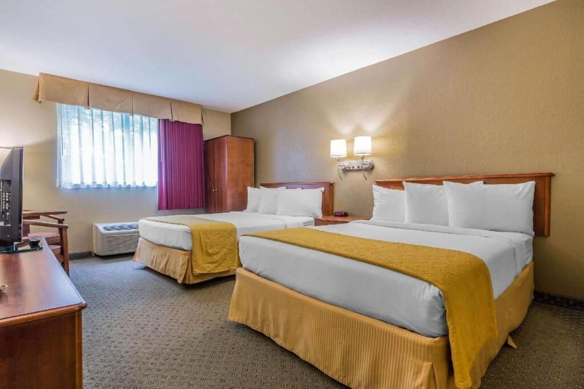 A hotel room with two beds, a desk, a television, and a window with curtains.