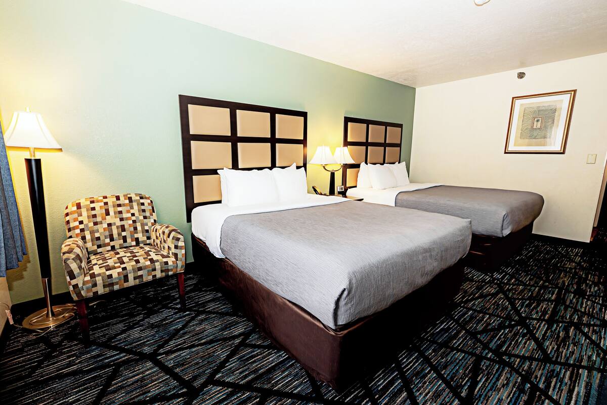 Een hotelkamer met een groot bed, twee nachtkastjes, een gestreept fauteuil en een vloerbedekking.