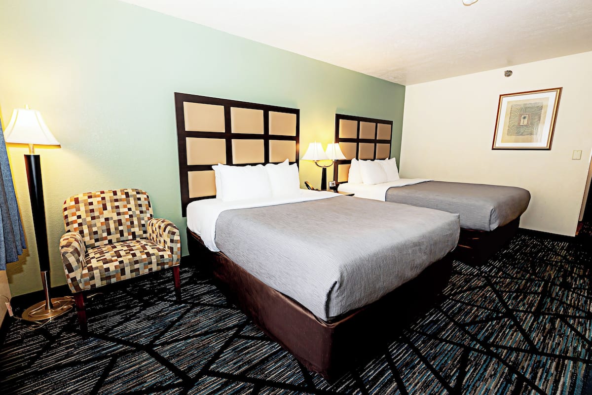 Habitación de hotel con una cama grande, dos mesitas de noche, un sillón estampado y suelo alfombrado.