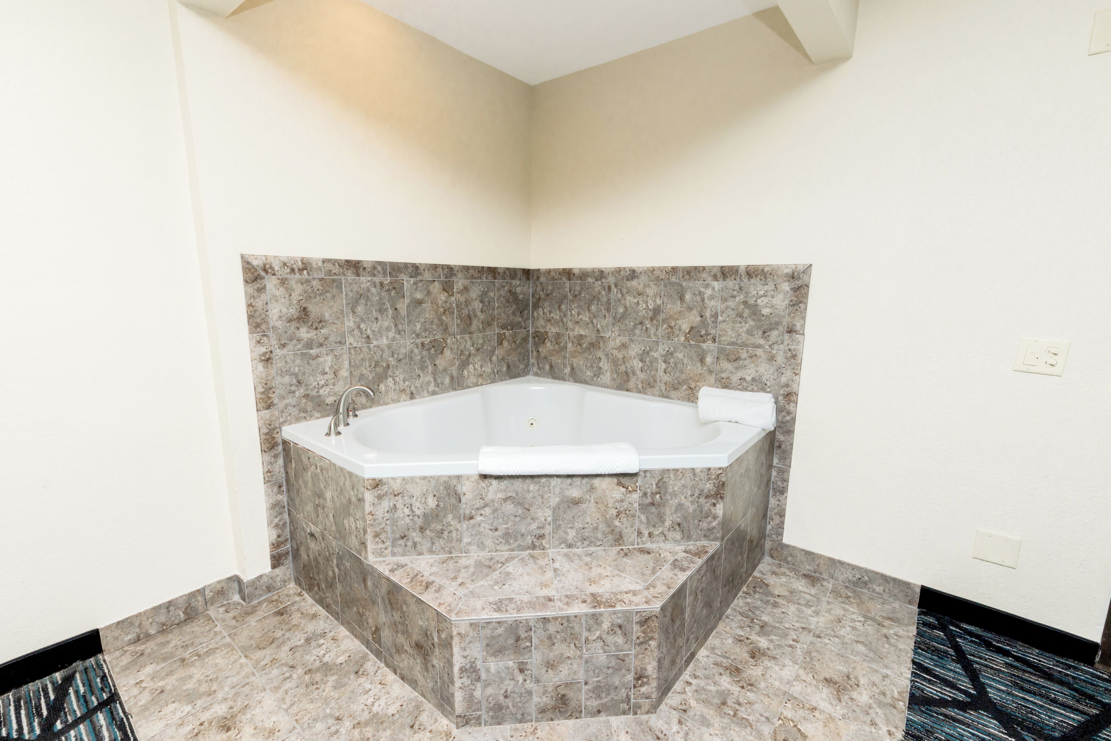 A corner bathroom with a freestanding bathtub, marble tiles, and a patterned rug.