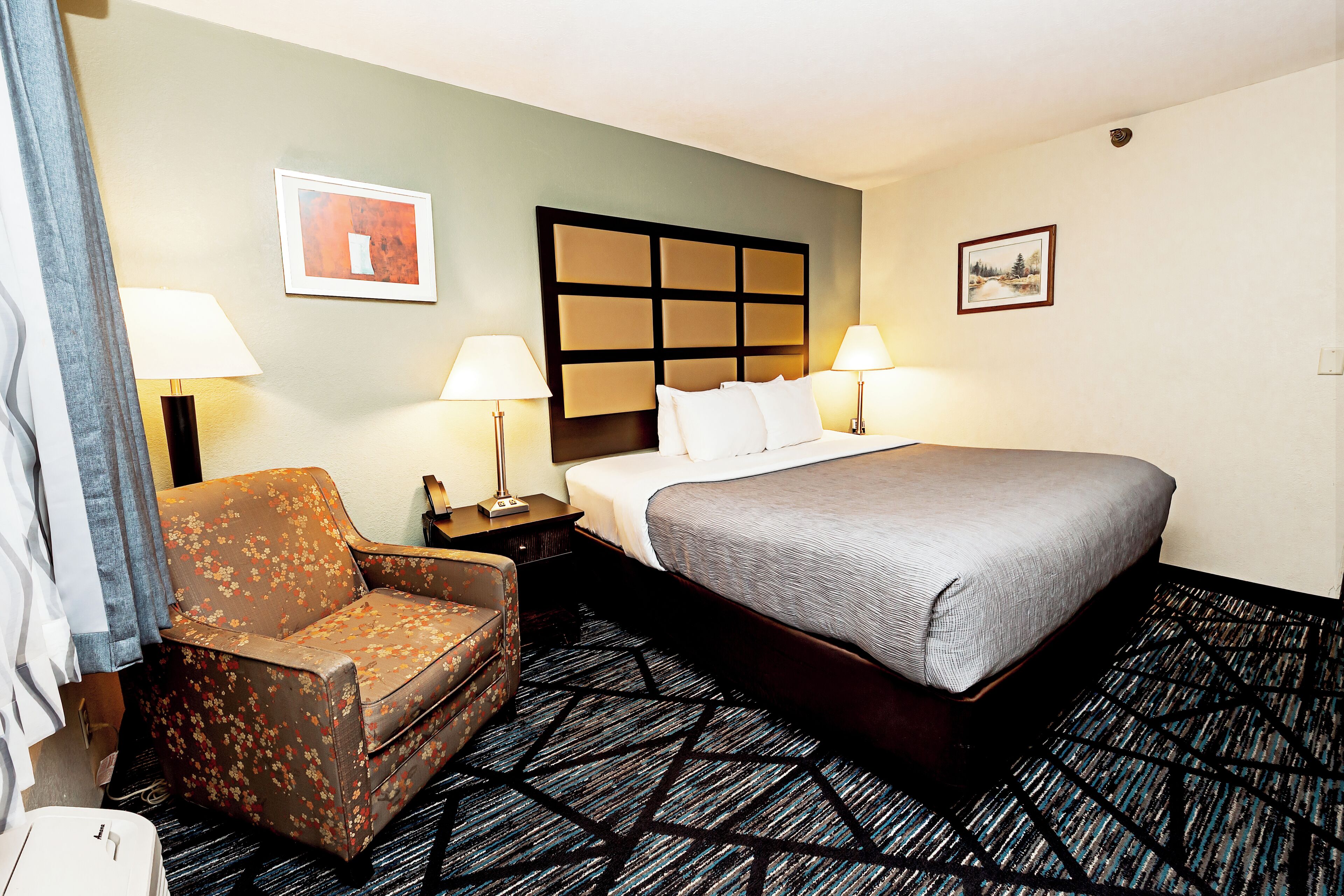 Ett hotellrum med en säng, en stol, två lampor och en sänggavel.