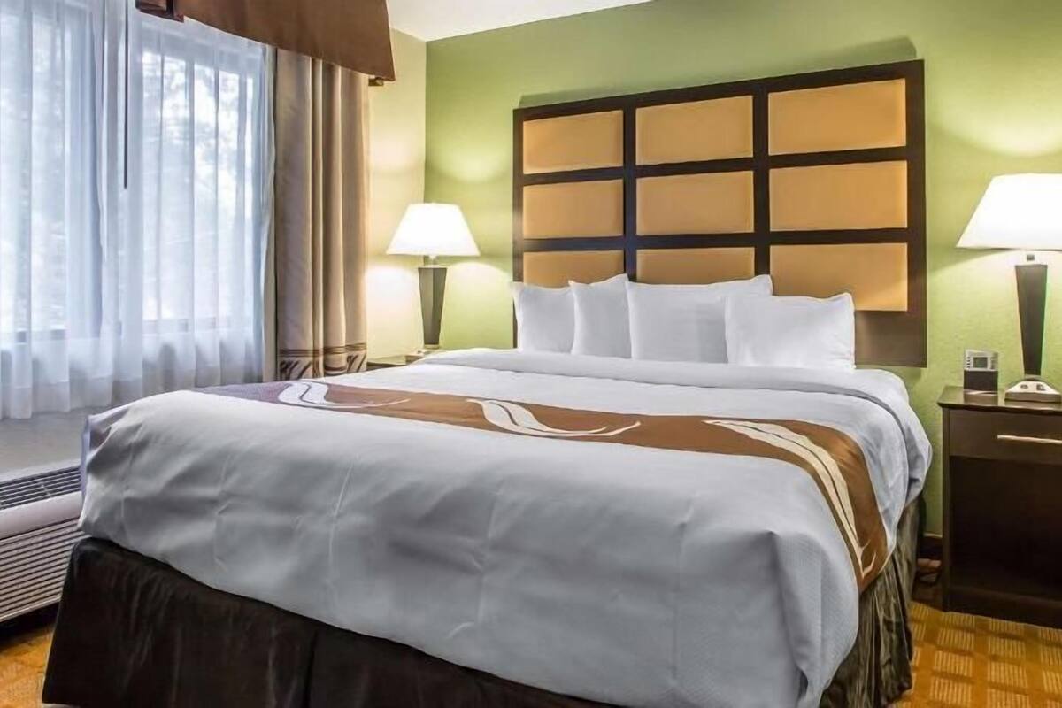Een hotelkamer met een bed, twee bedlampen, een nachtkastje en een raam met gordijnen.