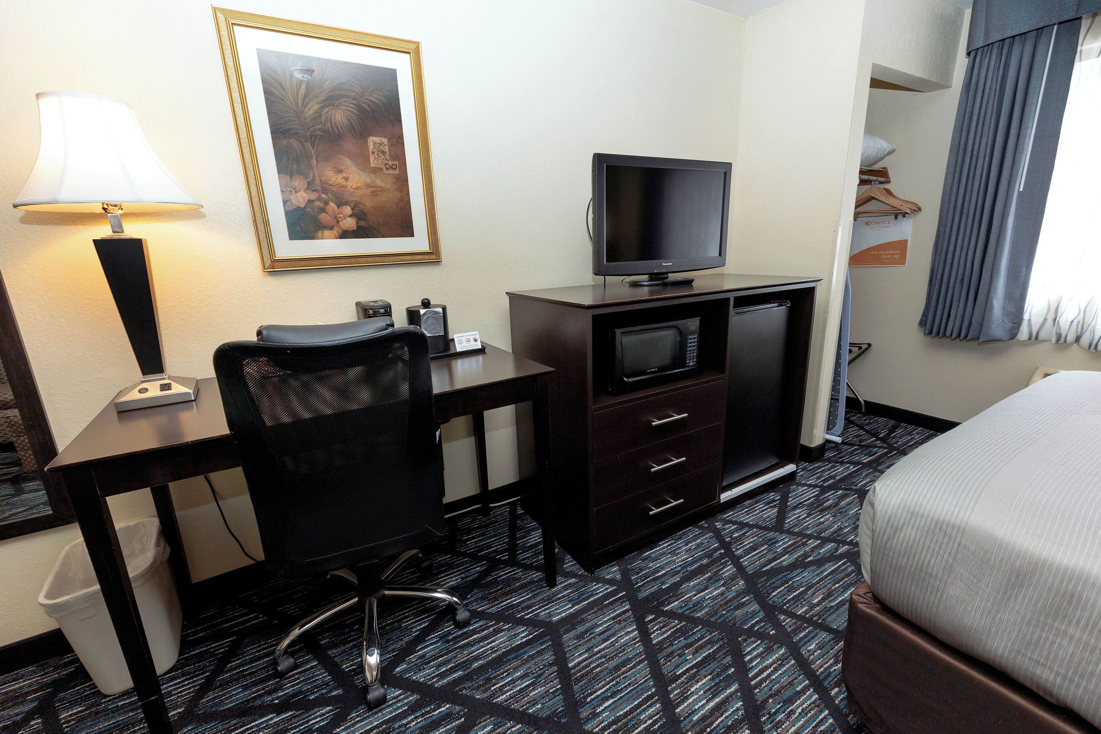 A hotel room with a desk, chair, television, and a bed.