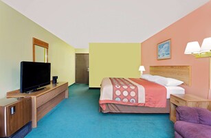 Habitación de hotel con una cama, un televisor sobre un mueble de madera, una mesita de noche, una lámpara y un cuadro en la pared.