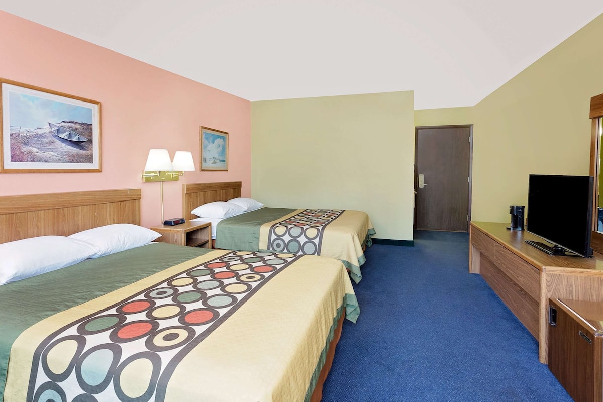 Habitación de hotel con dos camas, televisión, escritorio y un cuadro en la pared.