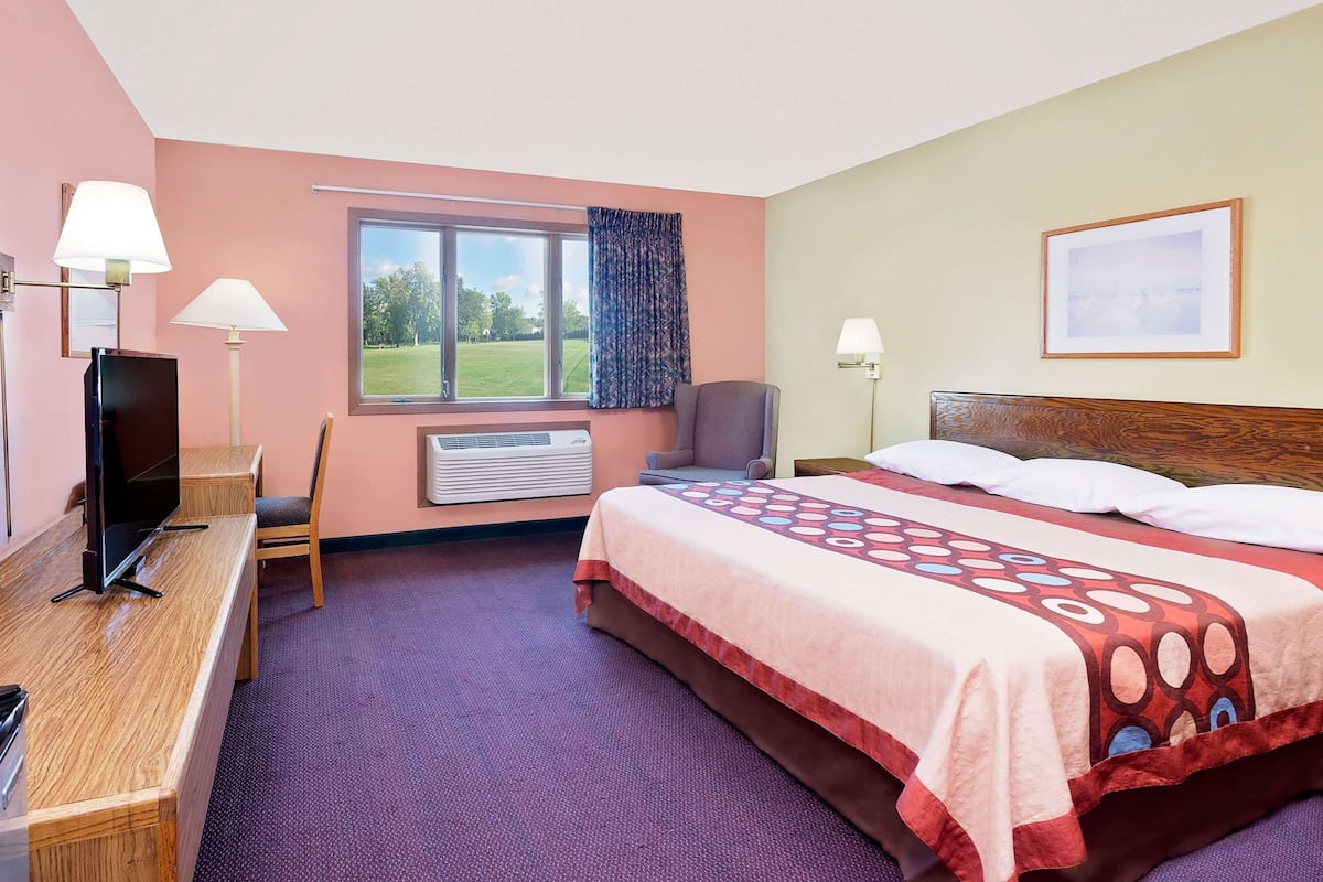 Habitación de hotel con cama, escritorio con televisor, una silla, ventana con vista y aire acondicionado.