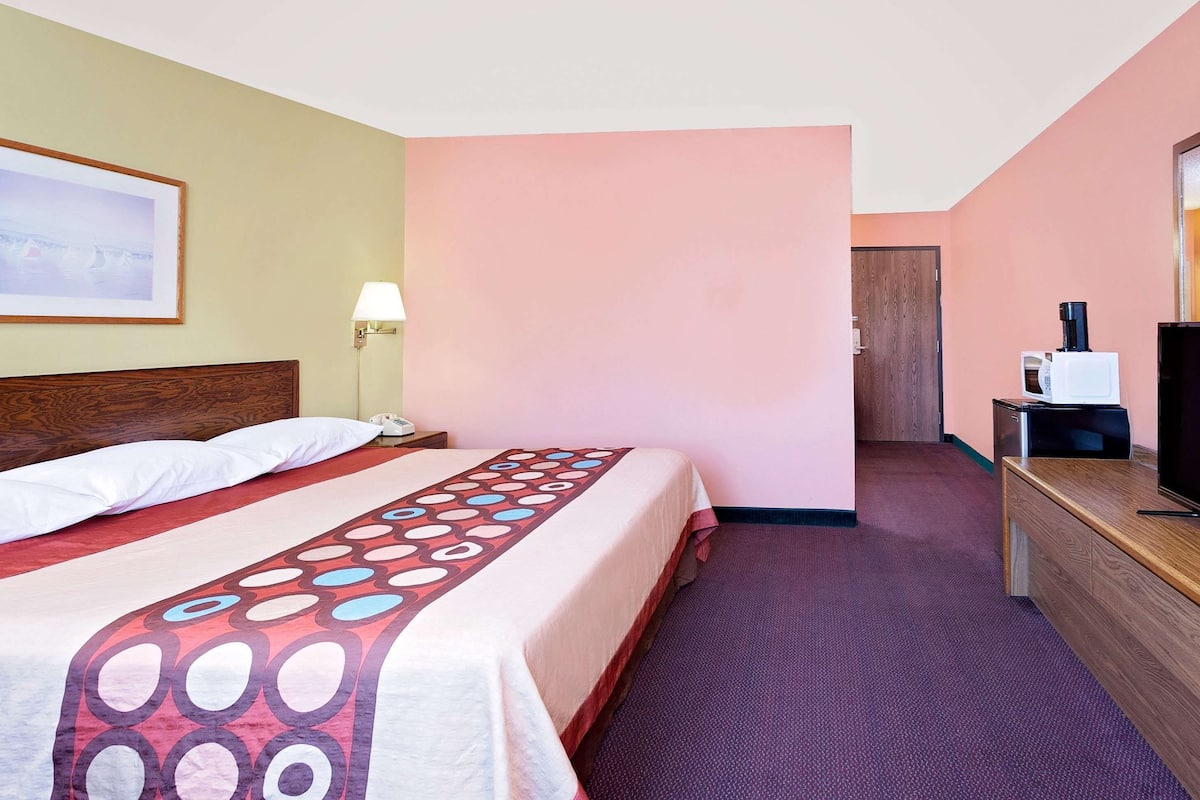 Una habitación de hotel con cama, escritorio con televisor, lámpara y puerta que da a otra habitación.