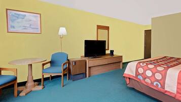 A hotel room with a bed, a desk with a television, a chair, a lamp, and a painting on the wall.
