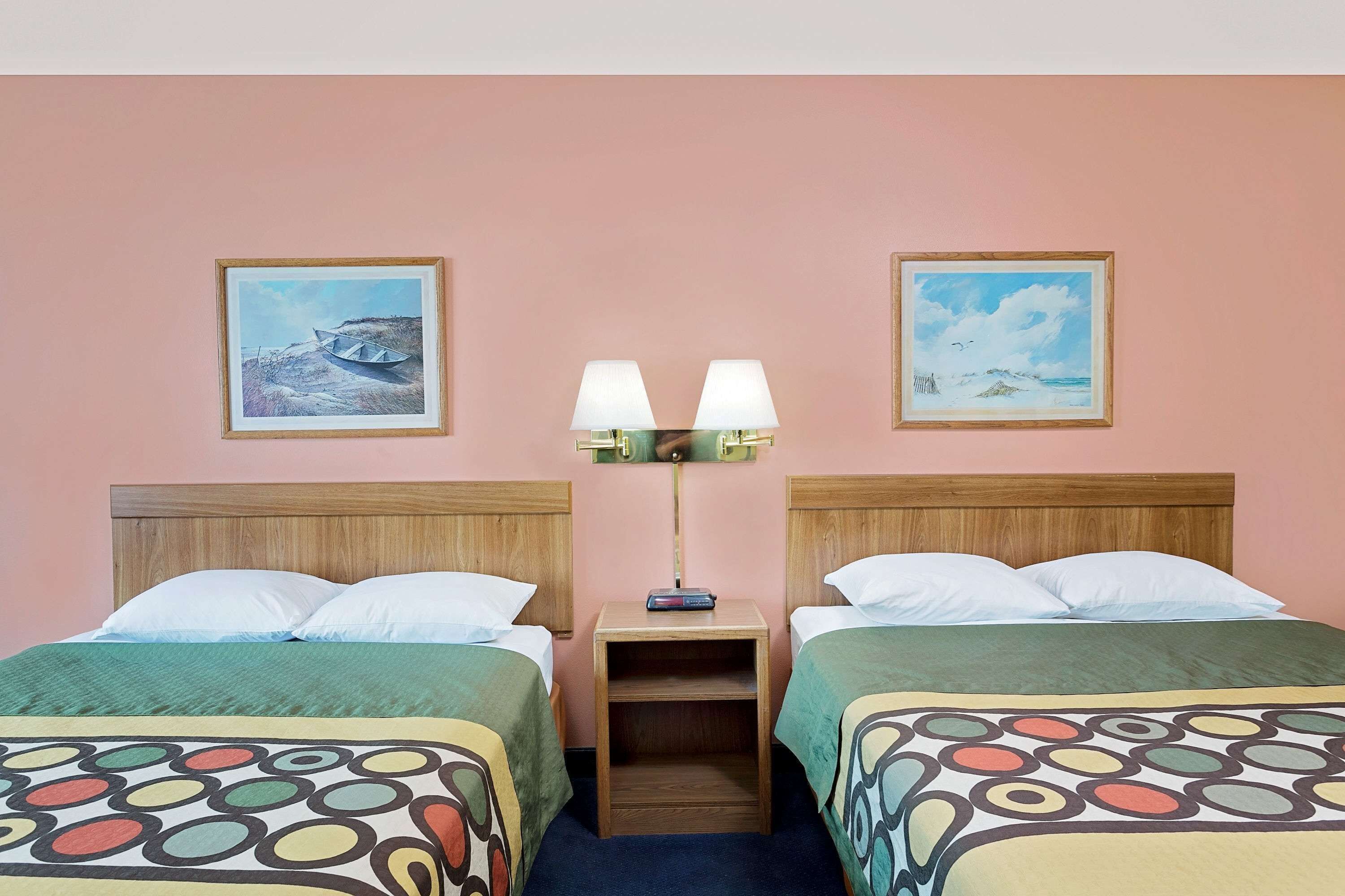 A hotel room with two beds, a nightstand with a lamp, and two framed pictures on the wall.