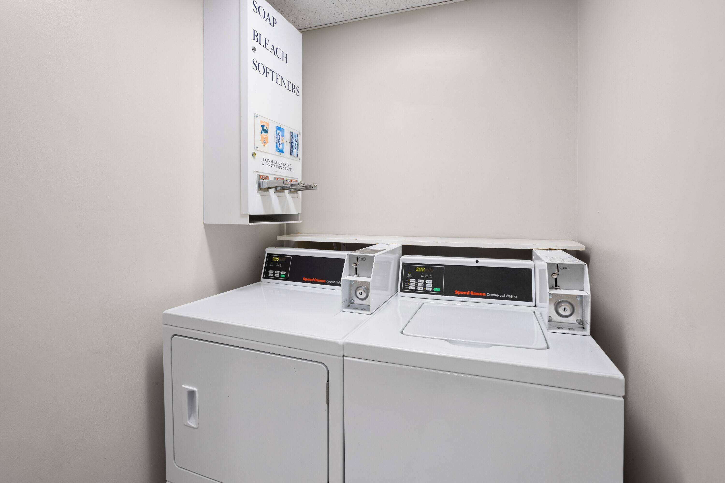 A laundry area with two front-loading washing machines and a wall-mounted dispenser for soap, bleach, and softeners.