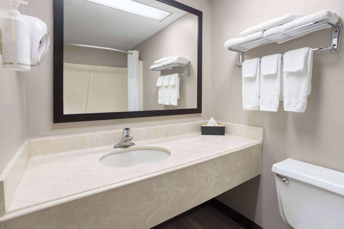 Un baño con lavamanos, espejo, toallero y retrete.