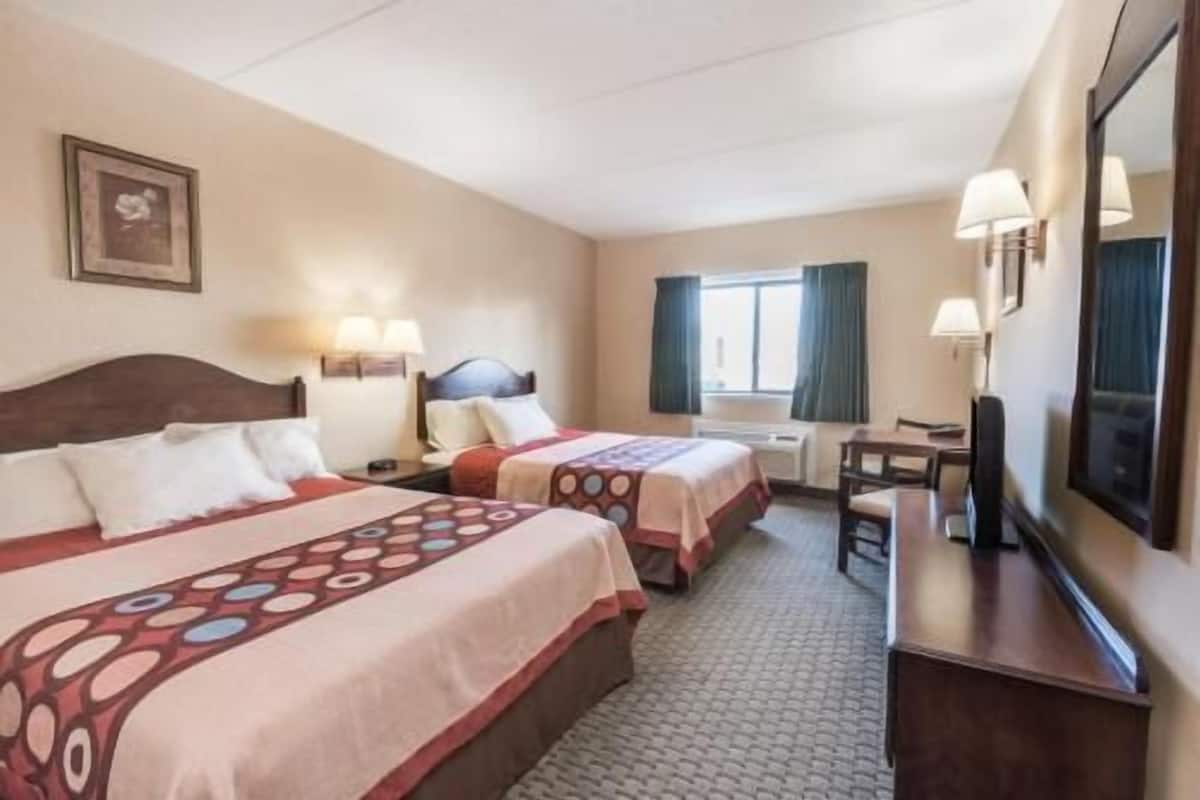 Une chambre d’hôtel avec deux lits, un bureau, une chaise, une télévision et une fenêtre avec des rideaux.