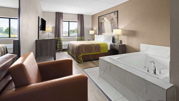Una habitación de hotel con una cama grande, un rincón de descanso con sofá, una bañera y un televisor en la pared.