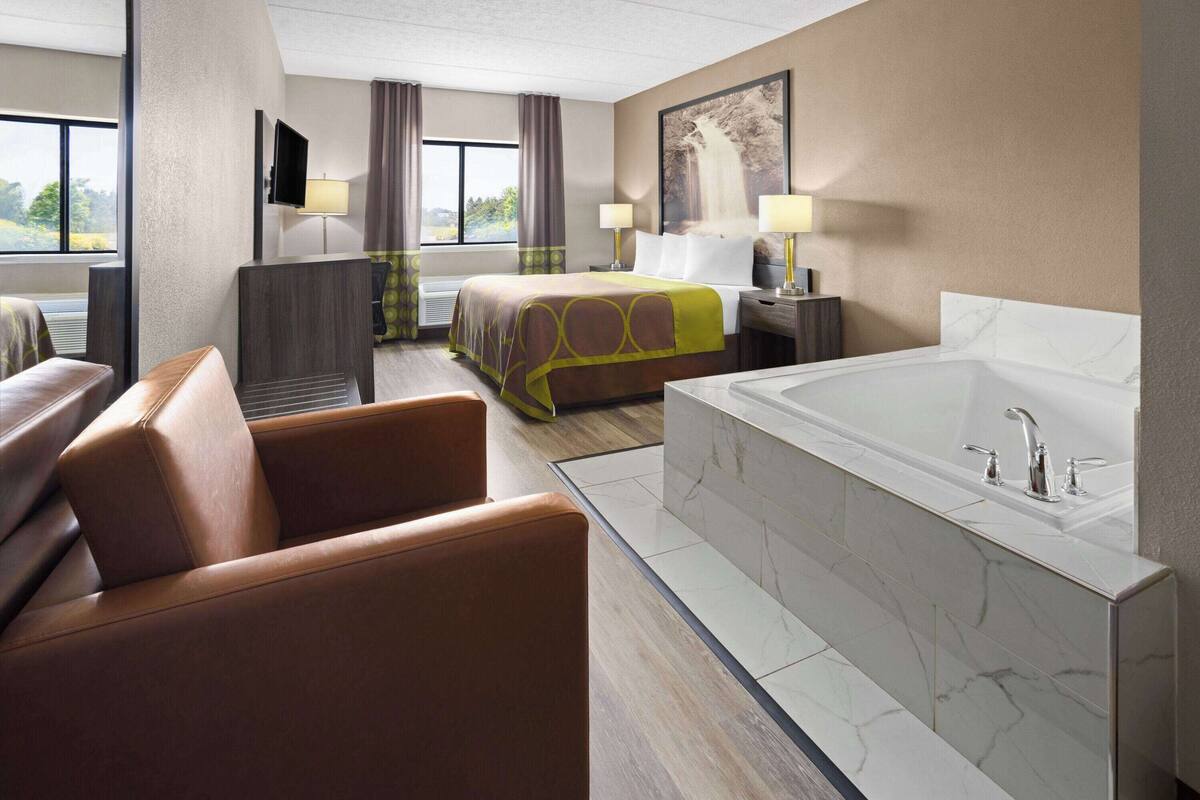 Una habitación de hotel con una cama grande, un rincón de descanso con sofá, una bañera y un televisor en la pared.