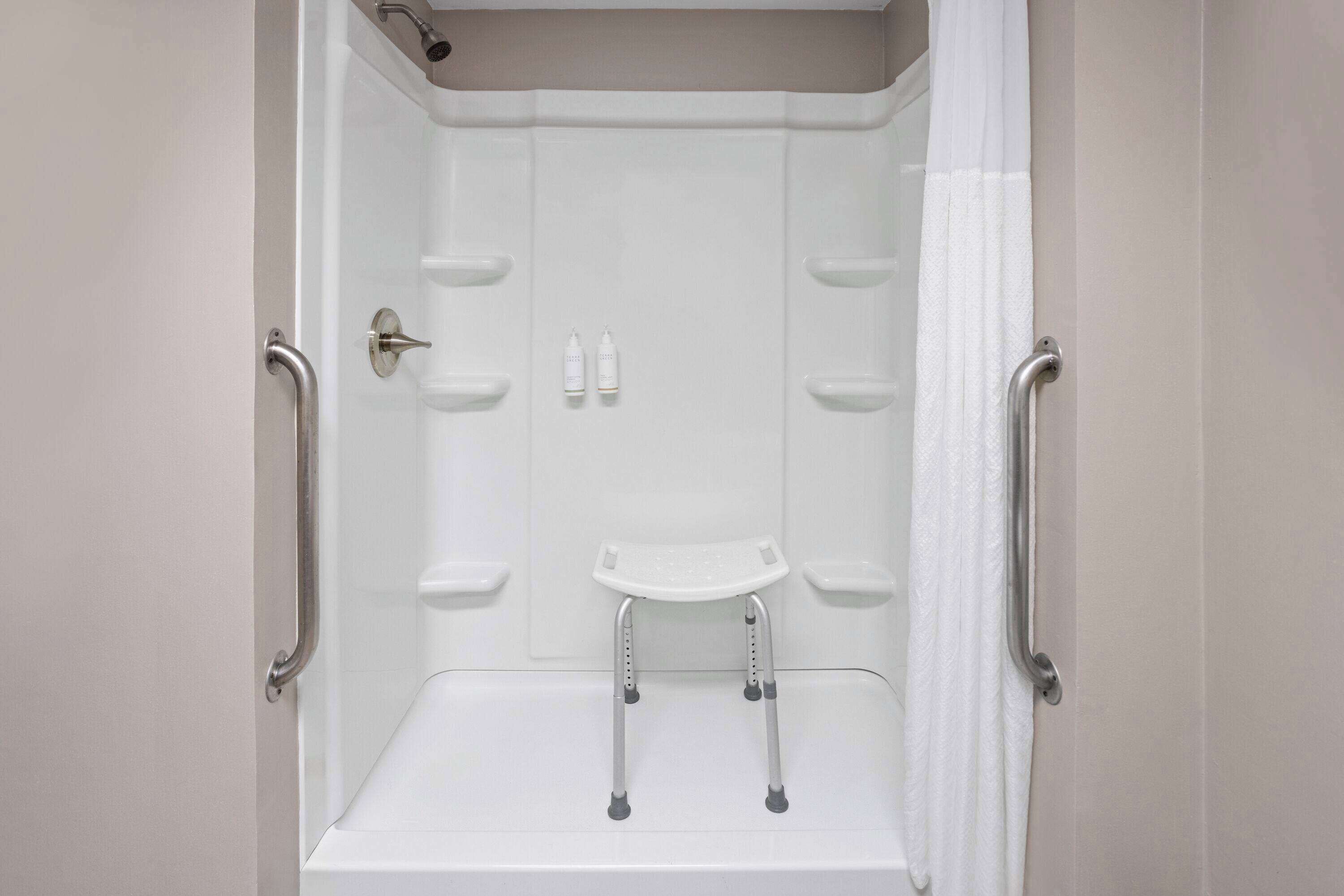 A white shower stall with a handheld showerhead, grab bars, and a white seat.