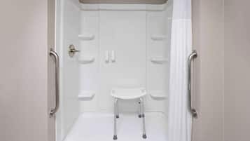 A white shower stall with a handheld showerhead, grab bars, and a white seat.
