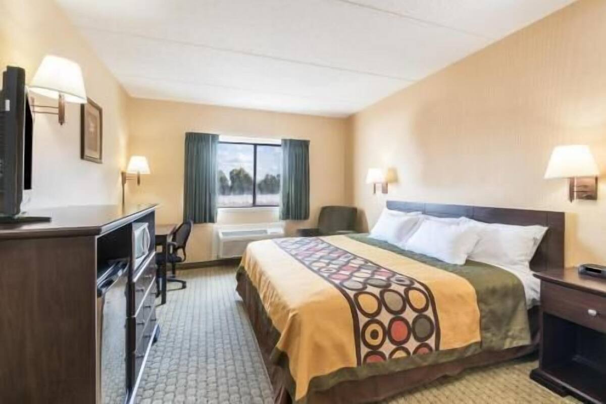 Habitación de hotel con cama, escritorio, silla, televisor y ventana con cortinas.