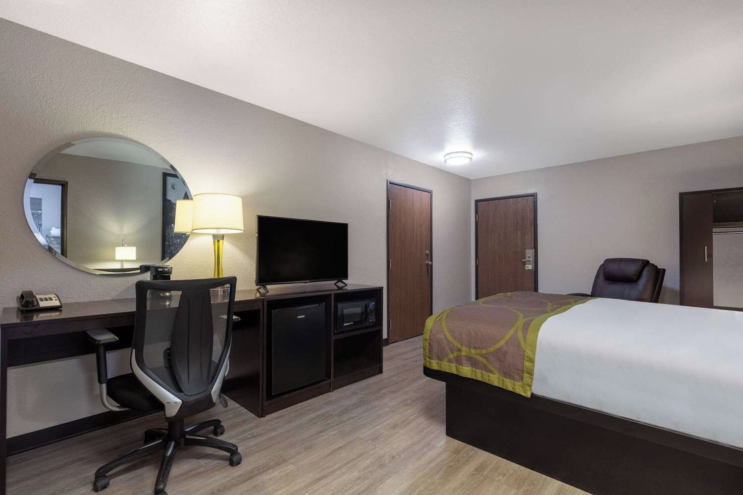 A hotel room with a bed, desk, chair, television, and a mirror.