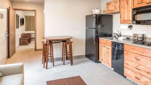 Cocina compacta con armarios de madera, un refrigerador negro, lavavajillas y un pequeño comedor con taburetes.