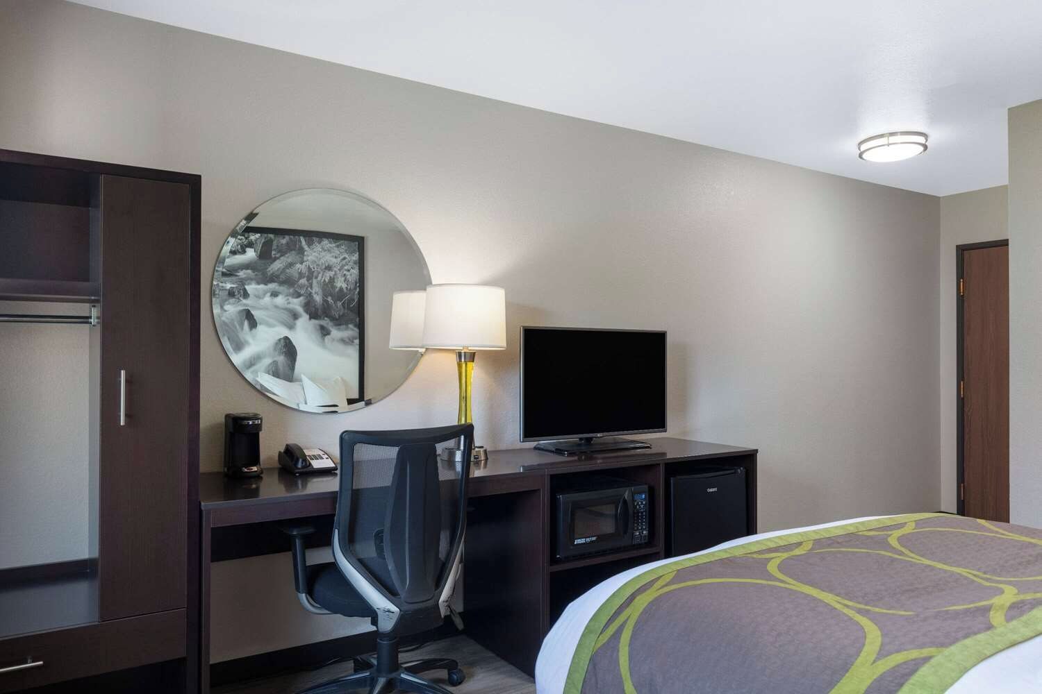 Een hotelkamer met een bed, een bureau met een computer, een televisie, een lamp en een spiegel.