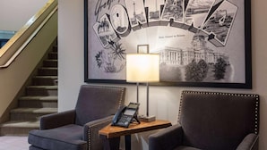 A lobby with a framed welcome sign, two armchairs, a small table with a phone, and a staircase in the background. - Super 8 by Wyndham St. Regis (St. Regis)