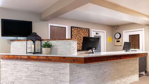 Zona de recepción con mostrador de piedra, televisor de pantalla plana, reloj y pared de troncos.