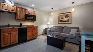 Un espacio habitable compacto con kitchenette, un sofá, una mesa de centro y un cuadro en la pared.
